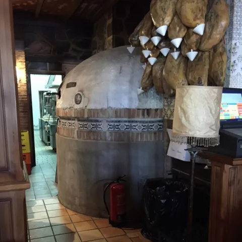 Horno tradicional junto a jamones curados en interior rústico.
