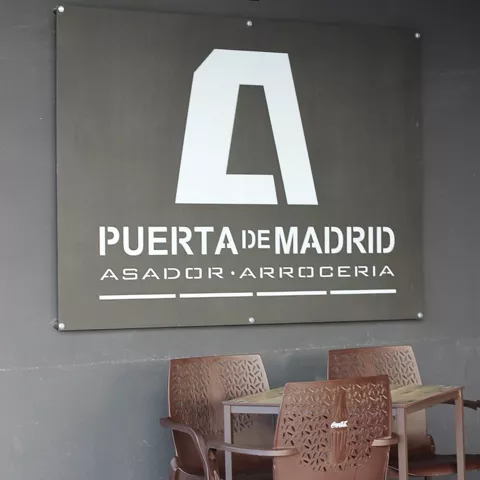 Cartel exterior en pared oscura con mesas y sillas de terraza.