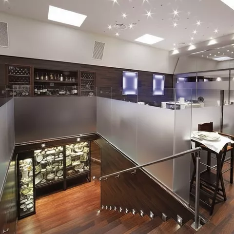 Interior de restaurante con escalera, vitrinas iluminadas y divisiones de cristal esmerilado.