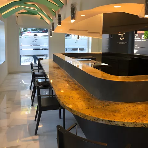 Barra de restaurante moderna con encimera dorada y techo geométrico verde