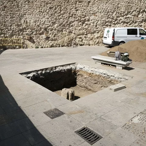Excavación rectangular junto a un muro antiguo de piedra.
