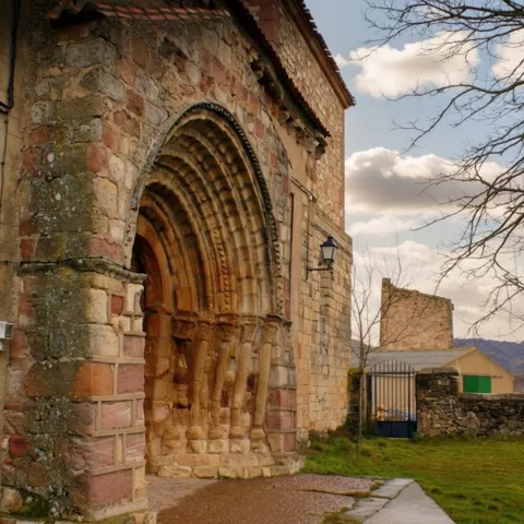 Portada románica de piedra junto a zona ajardinada