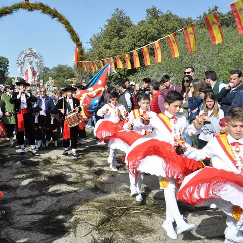 Niños bailando con trajes tradicionales bajo un arco decorado y banderas.
