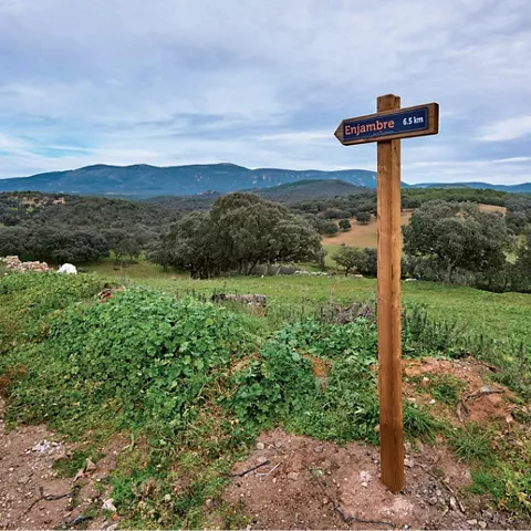 Señal de madera junto a sendero y colinas.