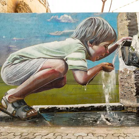 Mural de niño bebiendo agua de una fuente en un paisaje rural.