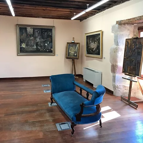 Sala con pinturas en paredes y diván azul en el centro.