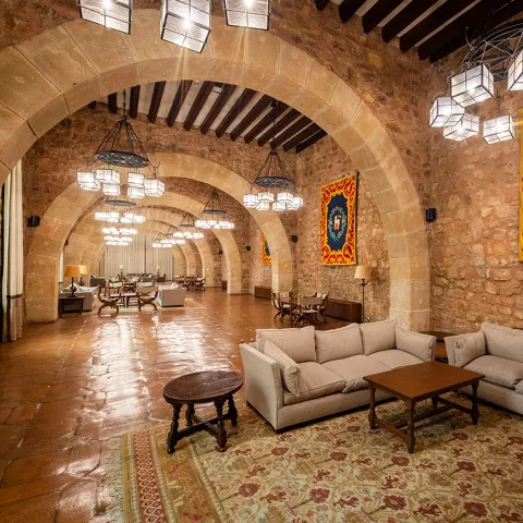 Gran salón de piedra con arcos y lámparas colgantes.