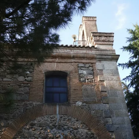 Detalle de una fachada de piedra y ladrillo que muestra un arco de medio punto cegado y una pequeña ventana bajo una cornisa.