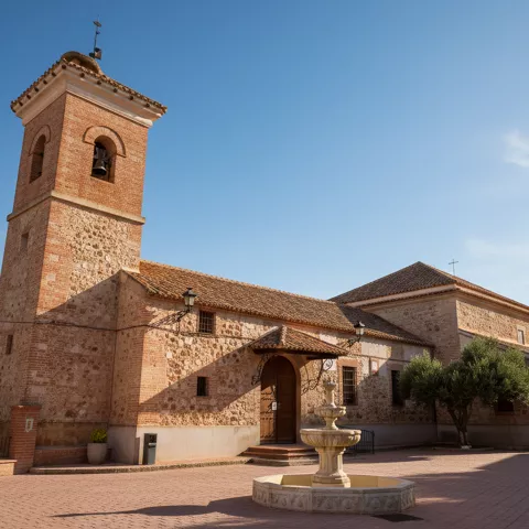 Panorámica de tejados de tejas en un pueblo, con una torre campanario de ladrillo destacando en el centro bajo la luz del atardecer.