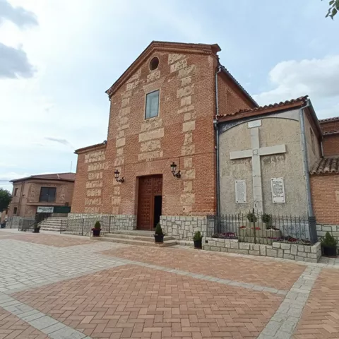 Fachada de iglesia de ladrillo junto a una cruz