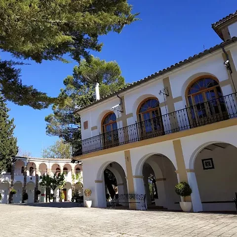 Plaza interior rodeada de galerías porticadas y pinos altos bajo cielo azul.
