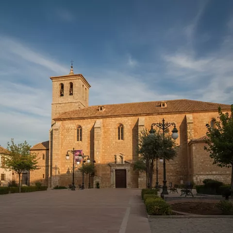Iglesia de piedra vista desde una plaza, con torre y farolas frente a la fachada.