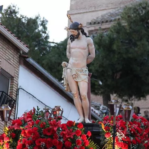 Imagen religiosa procesional rodeada de flores rojas al aire libre.