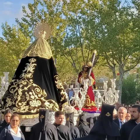 Procesión diurna con imágenes religiosas sobre andas rodeadas de nazarenos.