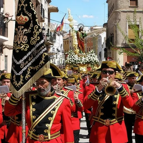 Banda uniformada encabeza procesión con imagen religiosa sobre andas.