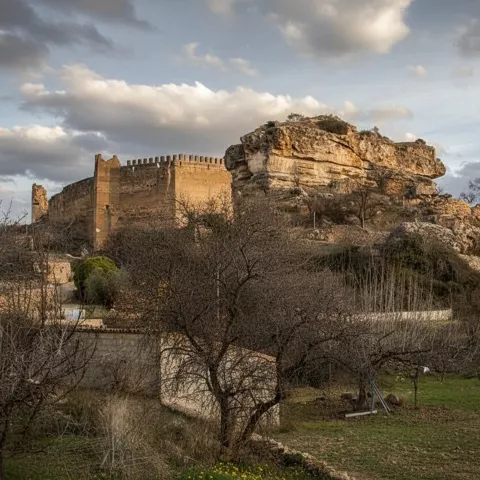 Castillo medieval de Socovos sobre un peñón rocoso, rodeado de árboles y paisaje rural al atardecer.