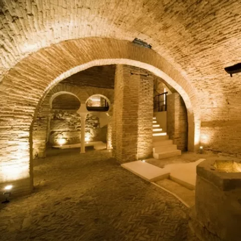 Detalle de arcos y columnas en sótano histórico con iluminación cálida ambiental.