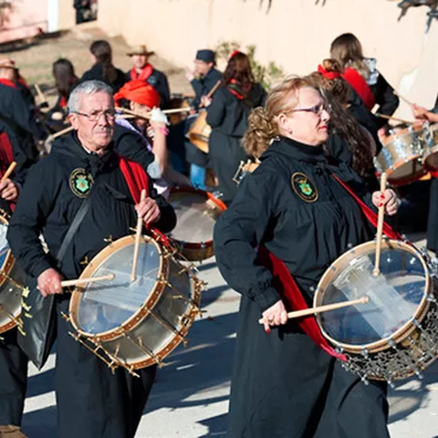 Dos tamborileros con túnicas negras y fajines rojos tocan tambores en la calle.