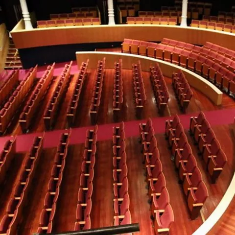 Interior de auditorio con filas de butacas de madera dispuestas en forma semicircular.