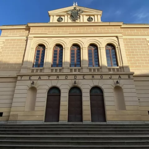 Fachada neoclásica de teatro con escalinata y grandes ventanales.