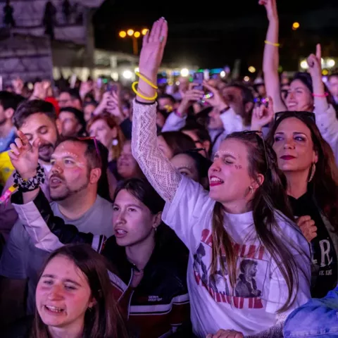Primer plano de asistentes cantando y disfrutando de un concierto nocturno.