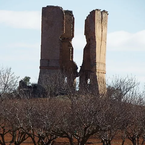 Ruinas de dos torres de mampostería entre campos.