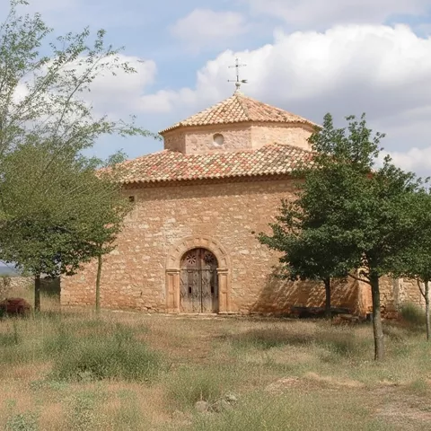 Ermita románica aislada entre árboles y campo abierto