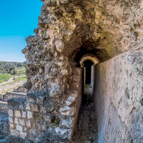 Galería excavada en piedra con arco y restos arqueológicos alrededor.