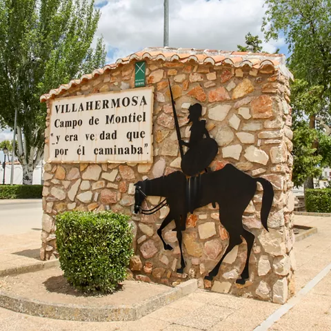 Monolito de piedra con silueta de jinete metálica en una rotonda ajardinada.