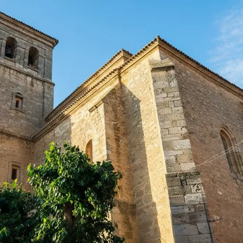 Una toma de ángulo bajo que captura la fachada de piedra texturizada de una gran iglesia con una torre de campanario cuadrada contra un cielo azul claro.