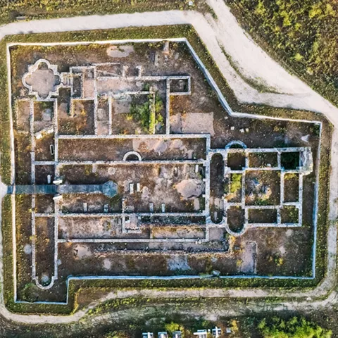 Vista aérea de un yacimiento con planta rectangular rodeado de caminos y vegetación.