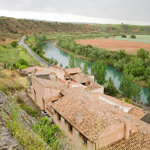Casas tradicionales junto a un río entre huertas y colinas suaves