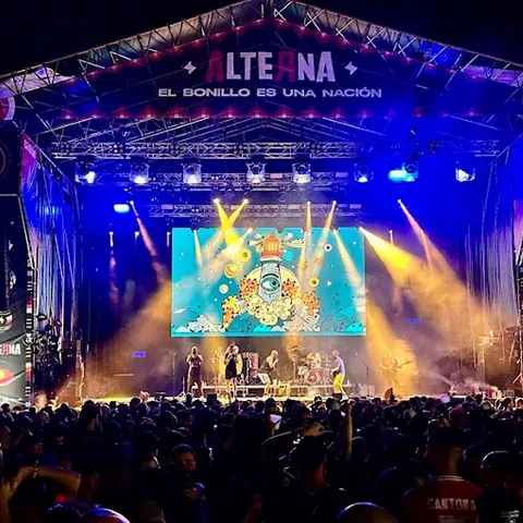 Escenario nocturno con luces de colores y público multitudinario.