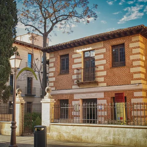 Fachada de ladrillo visto con ventanas verdes y verja de hierro en una calle tranquila.
