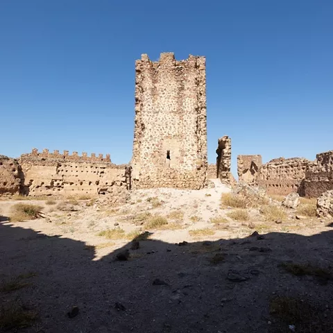 Patio interior de una fortaleza en ruinas con torre central de piedra.