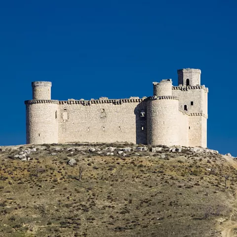 Castillo amurallado sobre colina con torres y cielo despejado.
