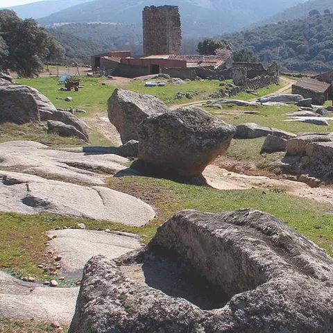 Paisaje rural con grandes formaciones rocosas y torre de piedra al fondo.