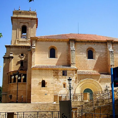Lateral de iglesia de piedra con torre cuadrada y muros macizos bajo cielo despejado.