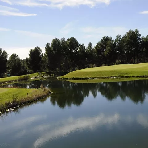Lago integrado en campo de golf con green y arbolado alrededor.