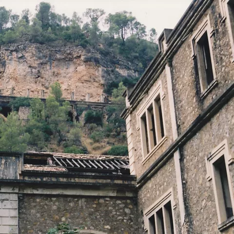 Edificio antiguo junto a un desfiladero con estructuras industriales en la ladera.
