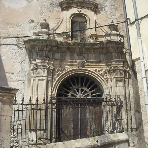 Portada barroca de piedra con balcón, reja de hierro y puerta arqueada.