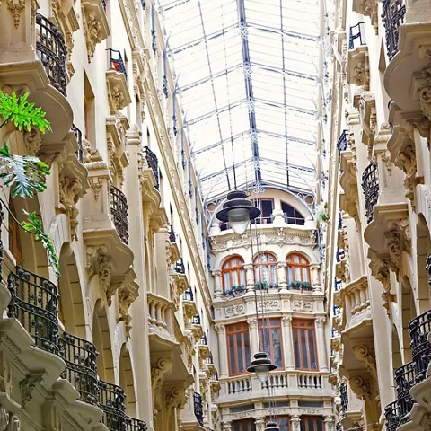 Vista interior de una galería con balcones, plantas y estructura acristalada superior.