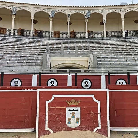 Barrera de madera roja con escudo y gradas vacías al fondo.