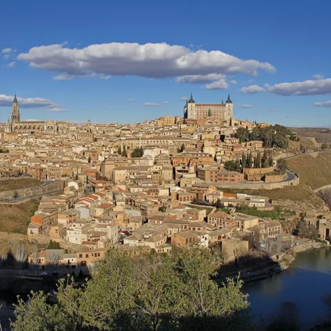 Una toma amplia de una ciudad histórica con edificios de piedra y un gran castillo en la cima de la colina, junto a un río que serpentea por el valle.