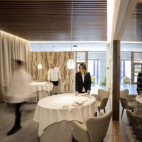 Sala elegante de restaurante con mesas vestidas y personal preparando el servicio.