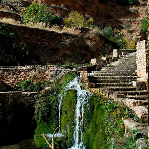 Cascada natural entre muros de piedra y escalones.