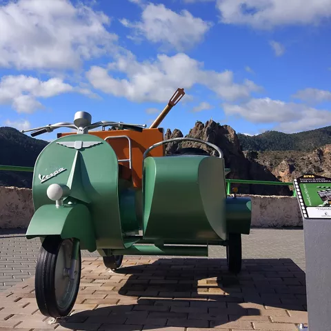Vehículo clásico de tres ruedas expuesto en un mirador con paisaje montañoso.
