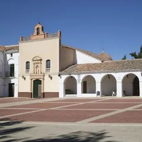 Plaza empedrada con edificio religioso y pórticos blancos bajo cielo despejado.