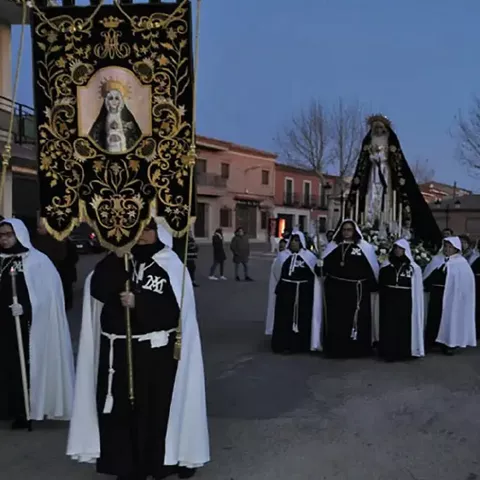 Formación de penitentes con túnicas oscuras y capas blancas al atardecer.