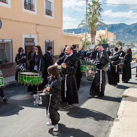 Grupo de personas tocando tambores y avanzando por una calle durante una celebración popular.